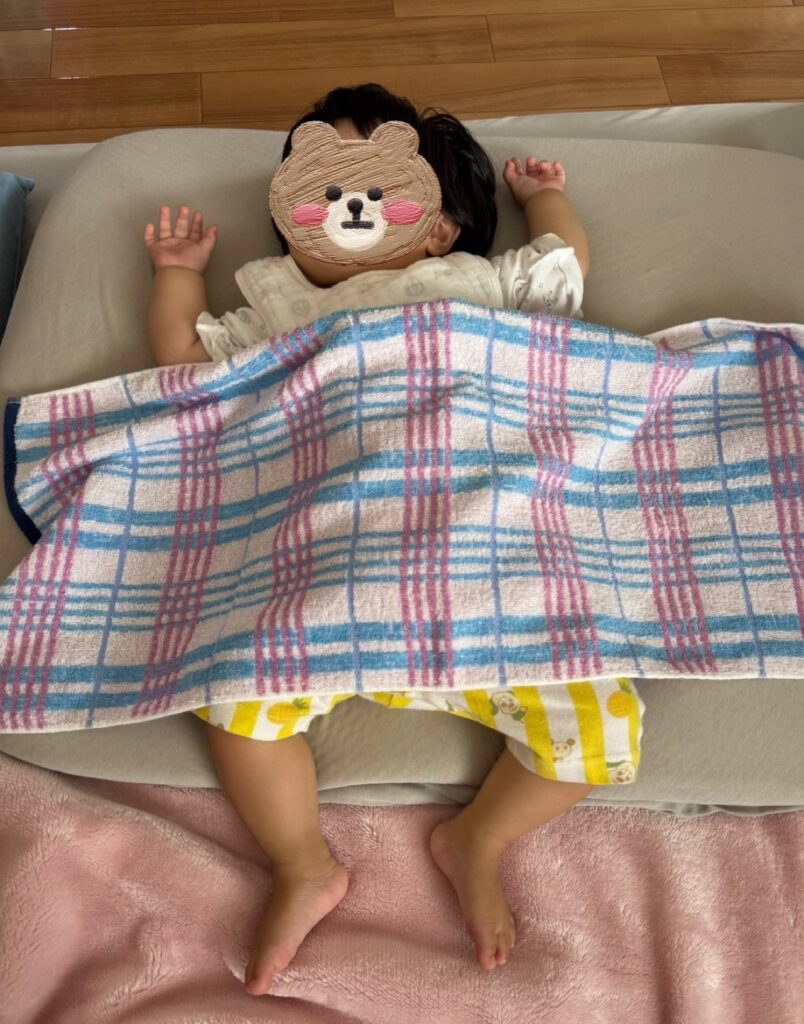 コンビ肌着姿で、お腹にタオルをかけて眠る赤ちゃん