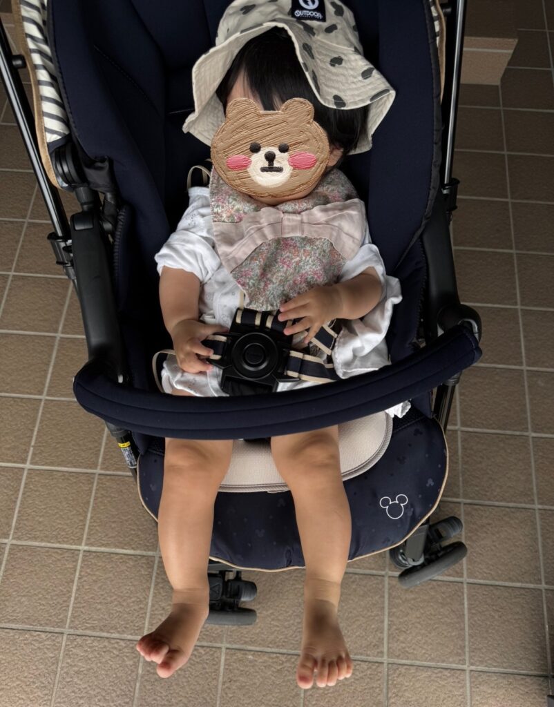 ベビーカーで、帽子とスタイ・コンビ肌着姿でお散歩する生後8ヶ月の赤ちゃん