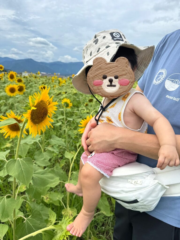 セパレートの服を着てひまわり畑で抱っこされる赤ちゃん