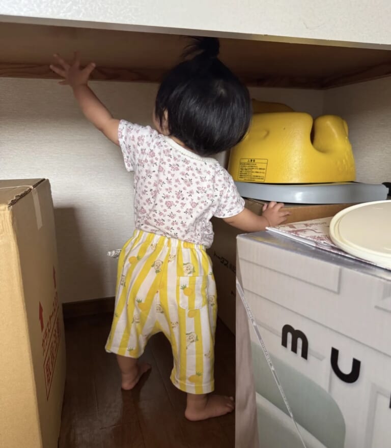 つかまり立ちで棚に手をのばす1歳の娘の後ろ姿